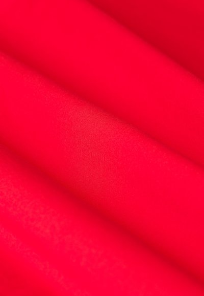 Roter Stoff mit glatter Textur, der ein schlichtes Design und einen subtilen Glanz aufweist, gefaltet, um Tiefe und einen geschichteten Eindruck zu zeigen.