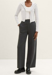 Szare spodnie o szerokich nogawkach w połączeniu z jasnoszarą prążkowaną kurtką na zamek z kapturem, noszone na białym topie na ramiączkach. Czarne masywne buty.