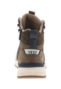 Chaussure montante en daim marron avec un accent bleu, col rembourré, semelle blanche et chiffres emboutis "1932" à l'arrière. Fini texturé.