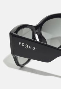Ochelari de soare negri cu un cadru voluminos și lentile gri. Bratul are un logo "vogue" din argint. Finisaj neted, lucios, cu margini rotunjite.