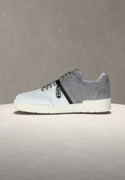 Χαμηλού τύπου αθλητικό παπούτσι με λευκό δερμάτινο μπροστινό μέρος, γκρι σουέντ πίσω μέρος, γκρι κορδόνια, πλαϊνό φερμουάρ και λευκή λαστιχένια σόλα σε ουδέτερο φόντο.