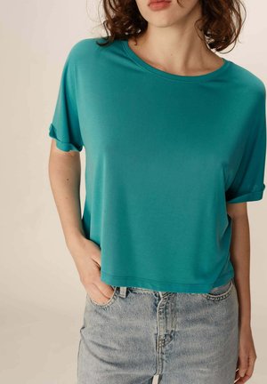 T-shirt court en teal en tissu doux, avec des manches roulées et un col en scoop, associé à un jean en denim délavé.