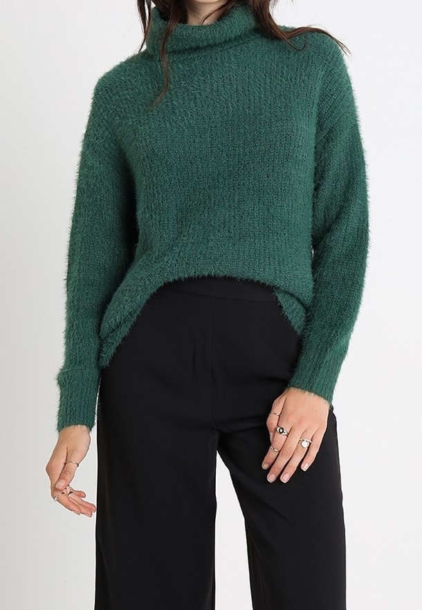 Vihreä, teksturoitu turtlenecksweater, jossa on rento malli, korkea kaulus ja hieman pidempi tausta, yhdistettynä mustiin korkeavyötäröisiin housuihin.