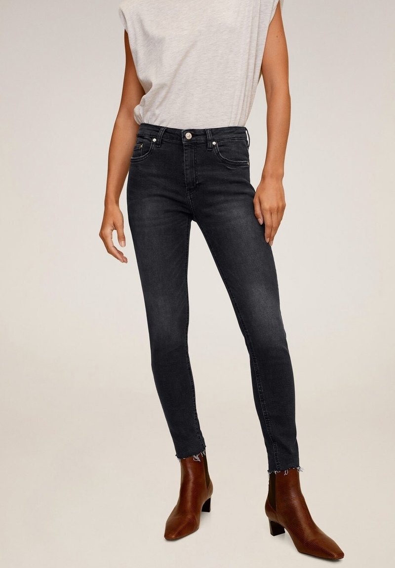 Schwarze Skinny-Jeans mit hohem Bund und ausgefranstem Saum, kombiniert mit einem hellgrauen ärmellosen Oberteil und braunen Stiefeletten mit strukturierter Oberfläche.