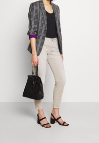 Grå rutig blazer med lila ärmdekor, svart tanktop, ljusbeige jeans och svart bucket-väska. Svarta klacksandaler.