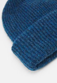Tumed sinine kootud beanie heledamate siniste aktsentidega. Ribitud tekstuur, volditud äär ja pehme villataoline materjal.