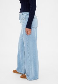 Svetlo modre široke kavbojke iz denima z visokim pasom, brezšivno zasnovo in rahlim obrabljenim videzom blizu žepov.