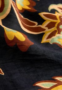 Audums ar tumšu fonu, kas rotāts ar ziedu rakstu dzeltenos, brūnos un zaļos toņos; mīksta tekstūra ar nedaudz savirknētu izskatu.