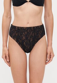 Bas de bikini taille haute en dentelle noire featuring des motifs floraux, une texture semi-transparente et une taille élastique pour un maintien sécurisé.