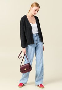 Svart stickad kofta, vit topp, ljusblå jeans med hög midja, röda sneakers och en vinröd axelväska med ett guldspänne.