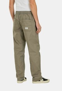 Helle khakifarbene Cargo-Hosen mit einem elastischen Bund, zwei Gesäßtaschen und einem rechteckigen Etikett. Tragen mit schwarz-weißen Sneakern.