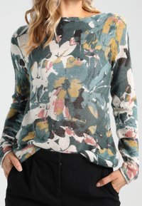 Blommig stickad tröja i teal, med abstrakta mönster i rosa, gult och svart. Långa ärmar, avslappnad passform, texturerad tyg.