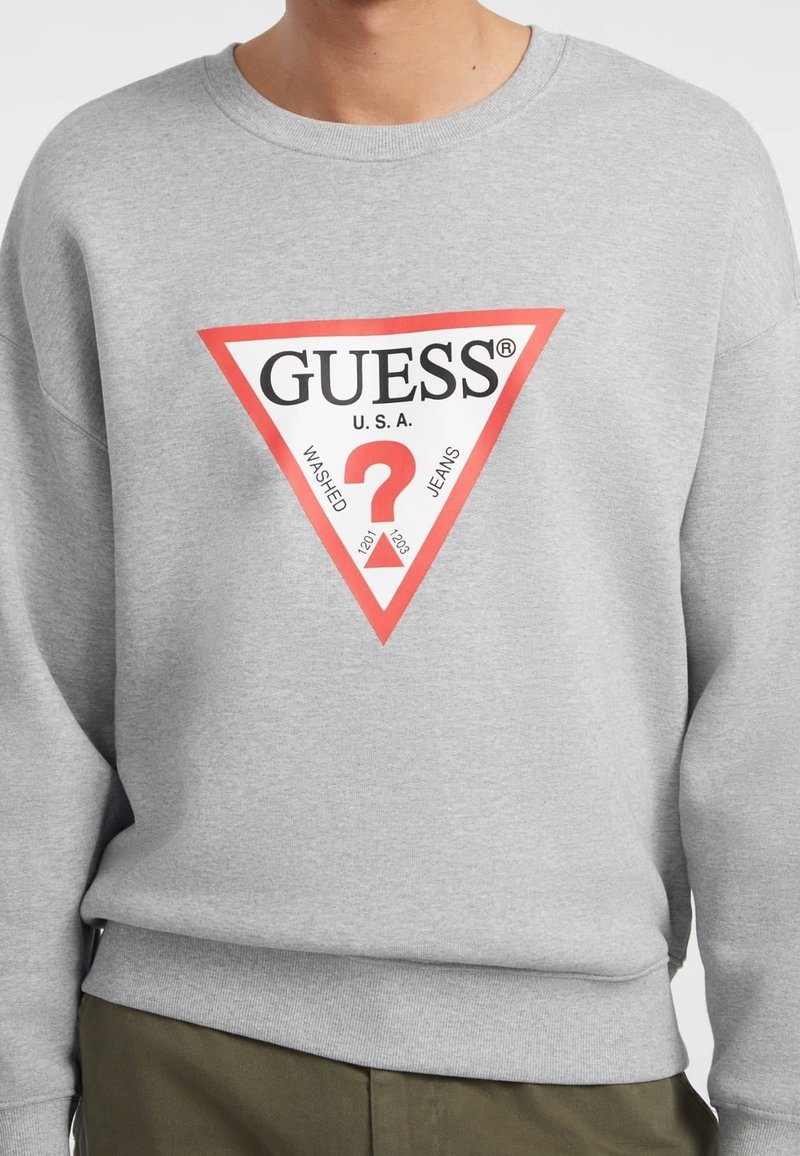 Felpa grigia a girocollo realizzata in tessuto, con un logo triangolare rosso e il testo "GUESS U.S.A" e "WASHED JEANS" in nero.