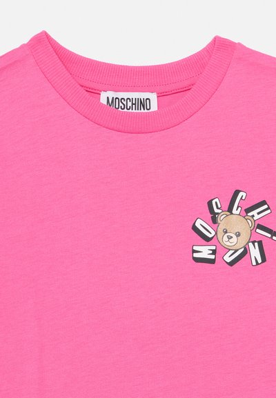 Розова тениска Moschino с релефна кръгла яка и малък графичен медвед на гърдите, заобиколен от името на марката.