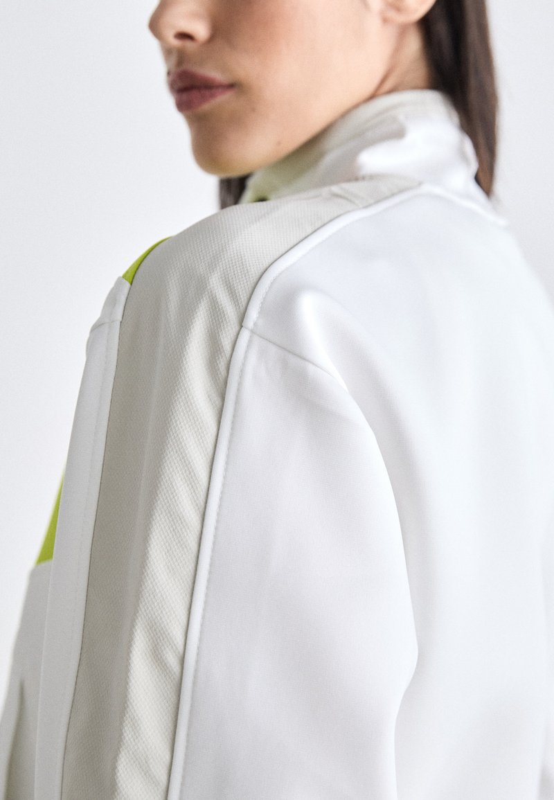Weiße Jacke mit strukturierten Akzenten in einem leuchtenden Limettengrün, mit hohem Kragen und strukturierten Schultern, die ein sportliches Design zeigt.