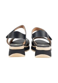 Sandalias de cuero negro con tiras cruzadas, un tacón grueso y una plantilla acolchada. Presenta una textura suave y un acento en la suela de color crema.