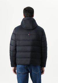 Navy puffer jacket with a hood, featuring quilted texture and horizontal seams. Small embroidered logo detail at the back.