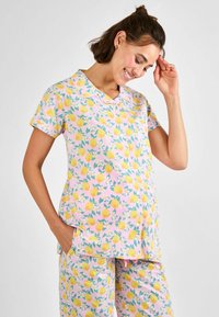 Lyhythihainen pyjama-asusetti, jossa on vaaleanpunainen tausta ja keltaisia sitruunoita sekä vihreitä lehtiä. Materiaali on pehmeää, ja siinä on kaulus ja taskut.