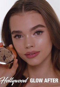 Bronzer compact dans un étui rond doré rose avec un motif d'étoiles ; le modèle présente le produit, affichant une peau éclatante et un maquillage léger.