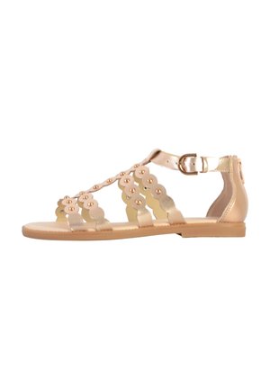Goldfarbene flache Sandalen mit einem T-Riemen-Design, das mit gewellten Mustern und dekorativen Nieten versehen ist. Schnallenverschluss am Knöchel.