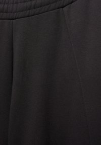 Gros plan sur un tissu noir avec une ceinture élastique et une couture visible sur la couture latérale d'un vêtement.
