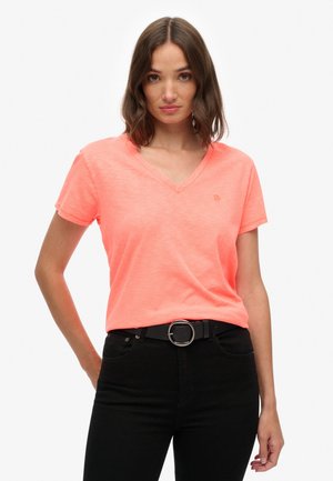 V-hals, kortemouwen t-shirt van helder neonroze stof, met een subtiele logo-detail, gedragen met een zwarte riem en donkere jeans.