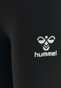 Leggings de sport noirs en tissu lisse et extensible, avec un logo "hummel" blanc et un design distinctif inspiré des abeilles.