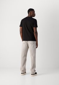 Mustapaita lyhyillä hihoilla, yksinkertainen muotoilu, yhdistetty vaaleanharmaisiin farkkuihin, slim fit, ja mustiin kenkiin, joissa on paksut valkoiset pohjat.