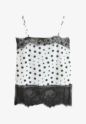 Camisole blanche avec des pois noirs, bordure en dentelle noire sur les bords supérieur et inférieur, et fines bretelles avec motif à pois.