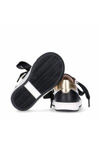 Sneaker bianco e nero con un accento dorato, dotato di lacci neri piatti, suola in gomma con battistrada a zigzag e tomaia in pelle liscia.