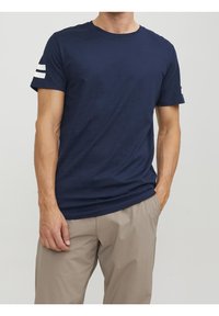 Camiseta de manga corta azul marino hecha de algodón, con cuello redondo y rayas horizontales blancas en la manga izquierda. Textura suave, corte relajado.