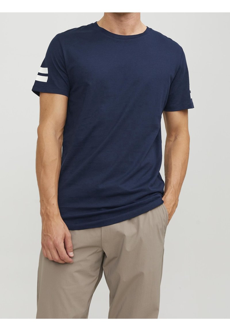 Camiseta de manga corta azul marino hecha de algodón, con cuello redondo y rayas horizontales blancas en la manga izquierda. Textura suave, corte relajado.