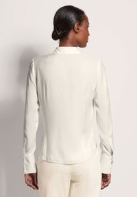 Witte blouse met lange mouwen, een gladde textuur en een licht gebogen zoom. Heeft knoopmanchetten en een klassieke kraag.