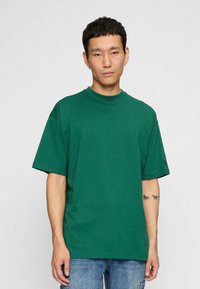 Groene katoenen T-shirt met een ronde halslijn en korte mouwen. Heeft een relaxed fit en subtiele branding op de mouw.