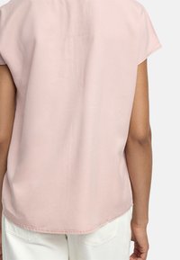 Bluzka z krótkim rękawem w kolorze różowym, z zaokrąglonym dołem i gładką teksturą, połączona z białymi spodniami z tylnymi kieszeniami.