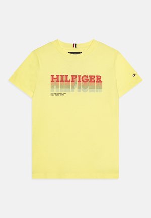 T-shirt en coton jaune avec le logo "HILFIGER" en dégradé rouge et bleu, manches courtes et col rond côtelé. Petit logo drapeau sur la manche.