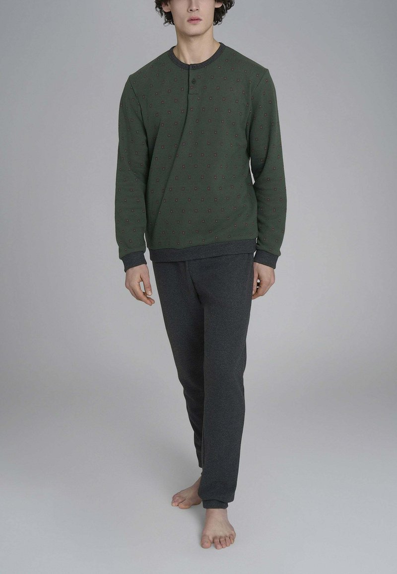 Felpa verde scuro con motivi geometrici rossi, colletto rotondo e maniche lunghe, abbinata a pantaloni grigi in stile aderente.