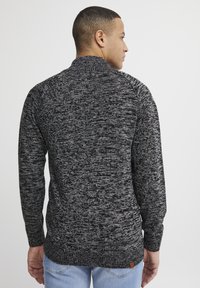 Suéter de punto en gris oscuro y negro jaspeado, con un cuello alto, mangas largas y un pequeño acento de logotipo de cuero en el dobladillo. Diseño de ajuste clásico.