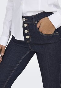 Donkerblauwe denim jeans met een hoge taille, vijf knopen sluiting en zijzakken met contrasterende stiksels.