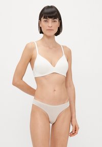 Biały stanik z cienkimi ramiączkami i głębokim dekoltem w kształcie V, w zestawieniu z cielistym, bezszwowym thongiem. Gładki materiał o minimalistycznym stylu.