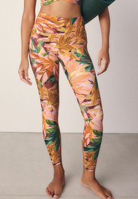 Legginsy w wzór z kolorowymi liśćmi w odcieniach pomarańczowego, różowego, zielonego i żółtego, z wysokim stanem i bezszwową strukturą.