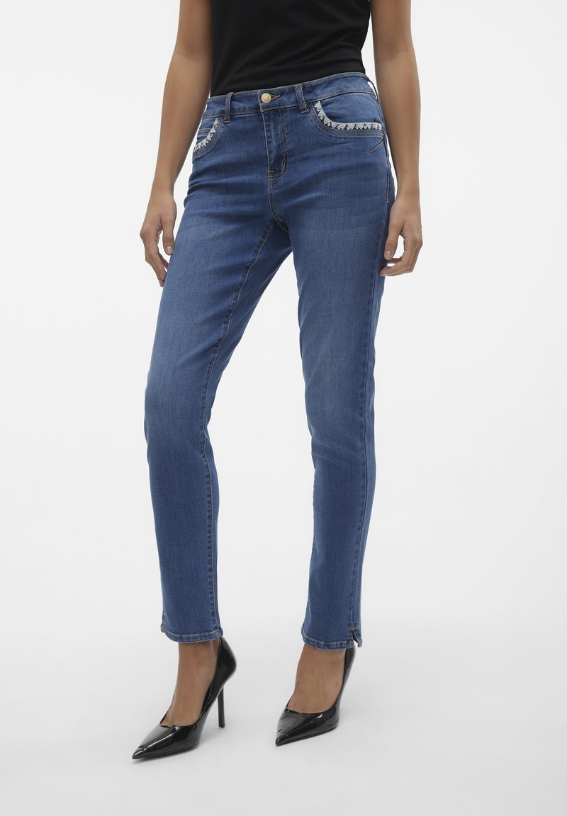 Jeans de mezclilla azul ajustados con una cintura de altura media, costuras en contraste, bolsillos decorativos y cremalleras en los puños.