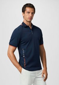 Námořnická polo košile se slim fit střihem, krátkými rukávy, oranžovými akcenty na límci a manžetách, s textem "HACKETT SPORT" podél strany.