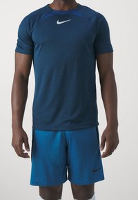 Nike kortärmad sporttröja i mörkblått, med en ljusare blå accent vid axlarna och en vit logotyp. Bärs med matchande blå shorts.