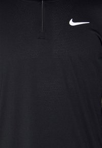 Mustapohjainen urheilupaita, jossa on neljännesvetoketju, hengittävä teksturoitu kangas pienillä reikiä, ja kontrastina valkoinen Nike-logo.