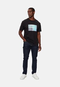 Camiseta de algodón negra con un gráfico rectangular en tonos de azul y blanco. Combinada con jeans de mezclilla oscura y zapatillas blancas.