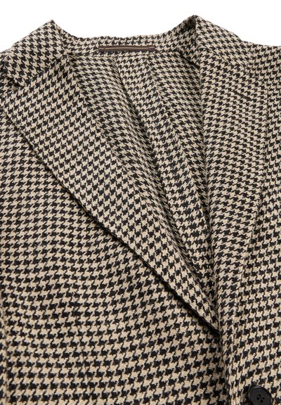 Braun-beiger Hahnentritt-Blazer mit breiten Revers und einem sichtbaren Knopf auf der unteren rechten Seite.