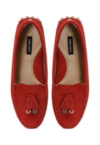 Mocassins en daim rouge avec un bout arrondi, dotés d'un accent à pampille et d'une couture décorative. L'intérieur présente une doublure lisse couleur tan.