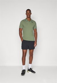 Grønn polo-skjorte med kontrastkrage, svarte shorts, hvite sokker og svarte treningssko. Tøyet ser glatt ut med minimal detaljering.