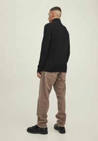 Maglione nero a coste con collo alto abbinato a pantaloni beige e scarpe nere. Il maglione presenta un design aderente e un collo alto.